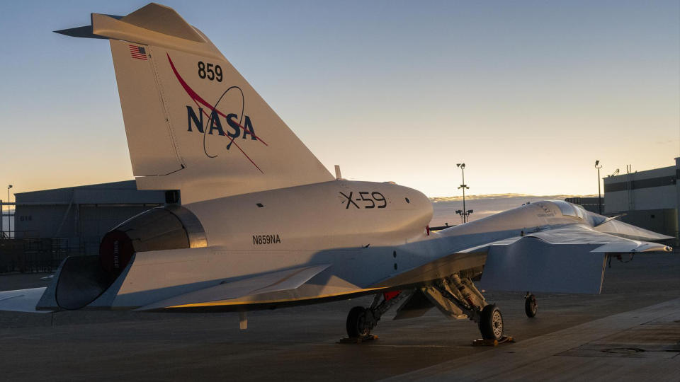 view of the back of a long blue-and-white jet with a colorful sunrise behind it