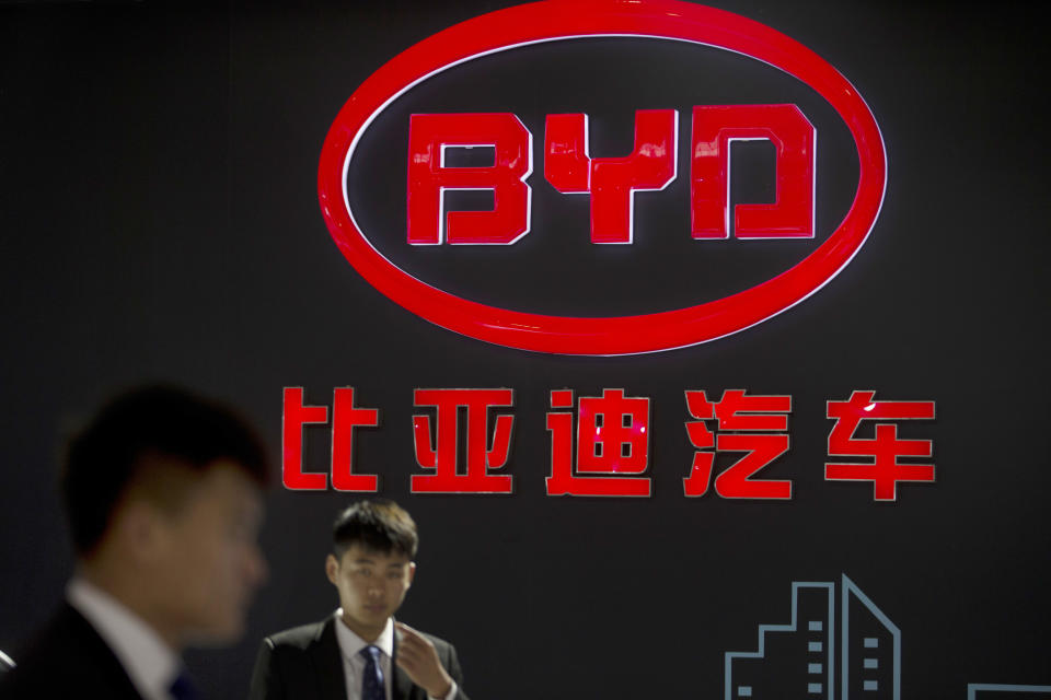 FILE - In this April 25, 2016, file photo, staff members stand near a logo for the BYD auto company as they wait for visitors at the Beijing International Automotive Exhibition in Beijing. The largest supplier of PPE to states this spring had never sold a single mask before the pandemic. But from mid-March to early June, Chinese electric vehicle maker BYD sold $930 million worth of masks and sanitizer to states. (AP Photo/Mark Schiefelbein, File)