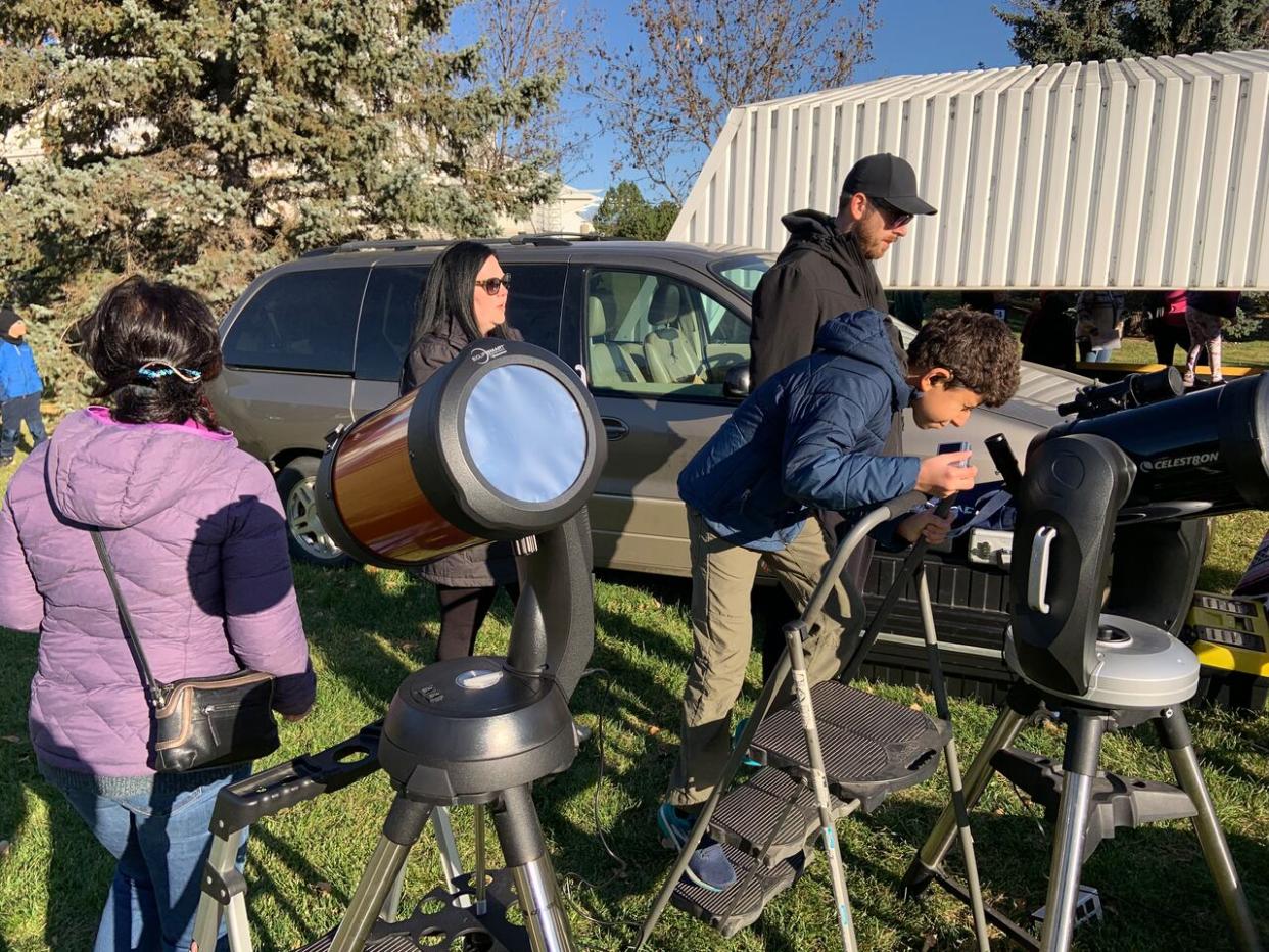 Edmonton Telus World of Science visitors view a partial eclipse in October 2023 with eclipse glasses and filtered telescopes.   (Submitted by Frank Florian - image credit)