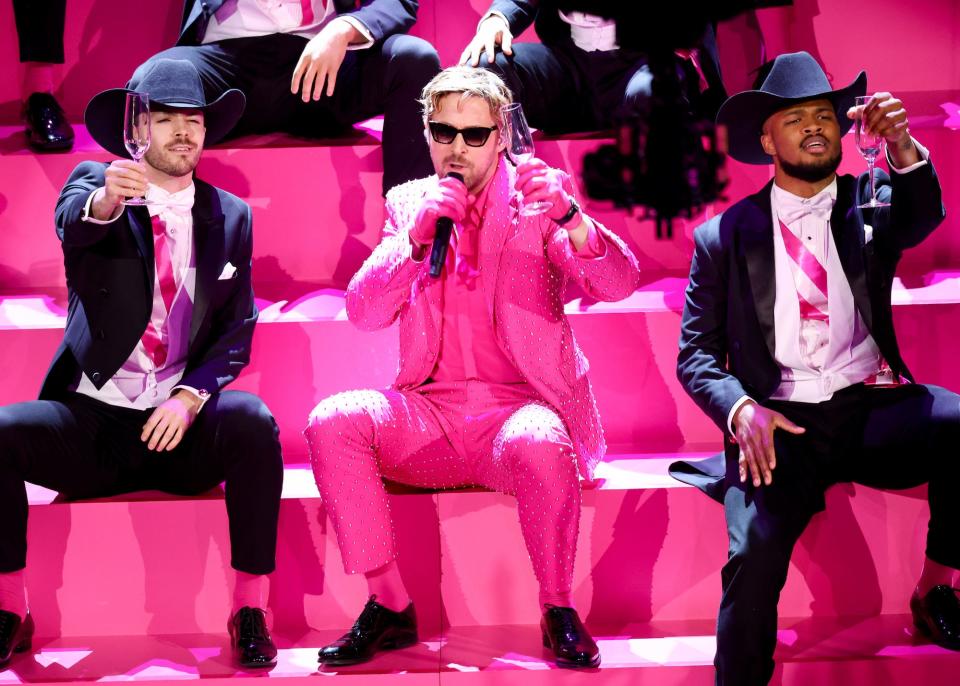 Ryan Gosling singing in a pink suit, holding up a Champagne glass, with dancers around him.