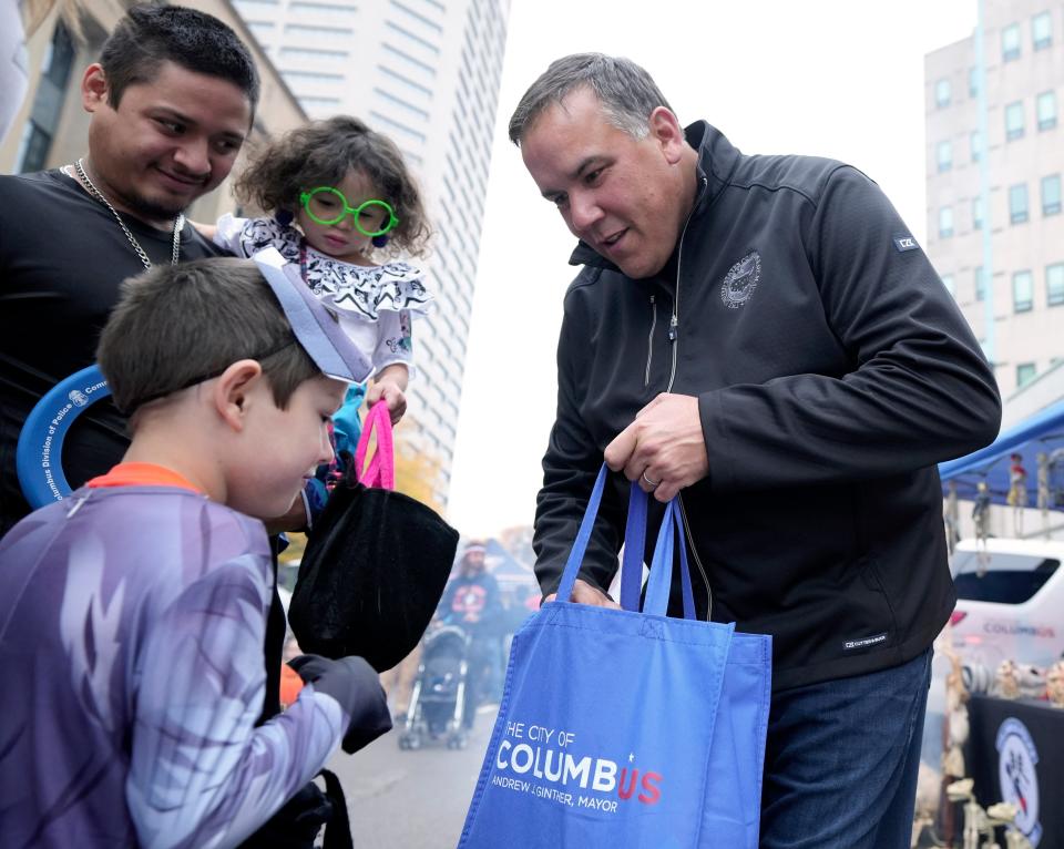 Oct. 29, 2023; Columbus, Oh., USA; 
Mayor Andrew Ginther passes out candy to Xavier Landaverde, 7, as his father Alex Landaverde and little sister Ally, 3, watch as Columbus Division of Police and the Columbus Division of Fire hosted their second annual trunk or treat event along Marconi Blvd. in front of Columbus Police Headquarters on Sunday.