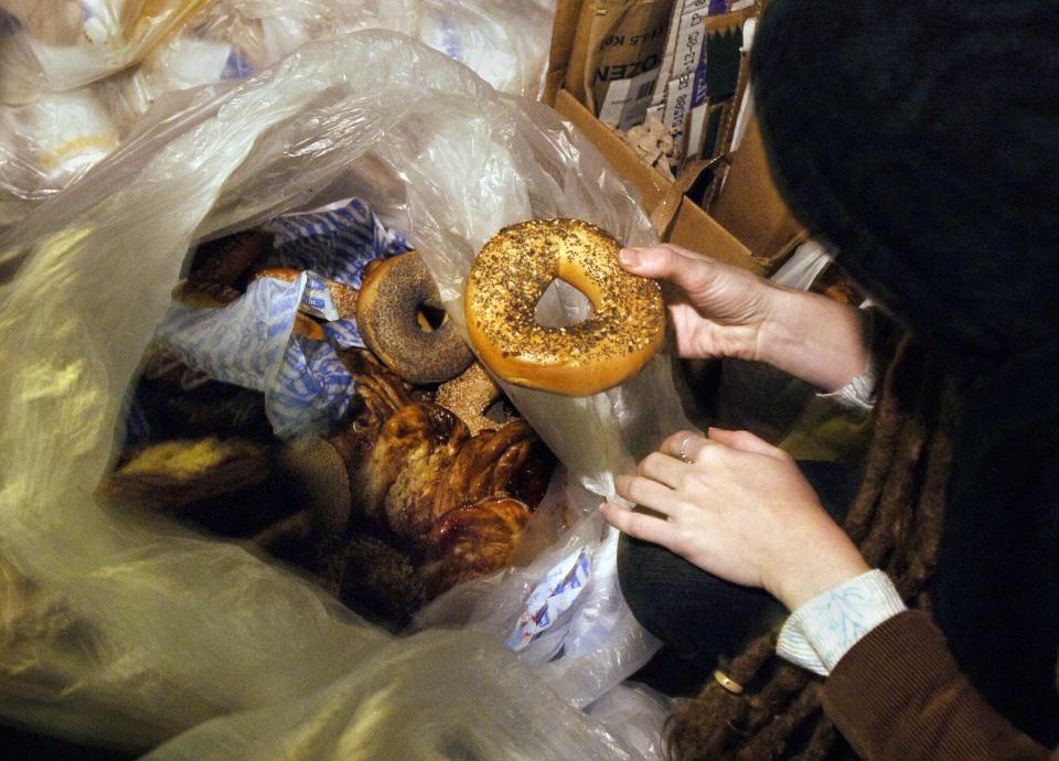 A freegan explores a trash bag full of pastries and bagels outside a New York City bakery.