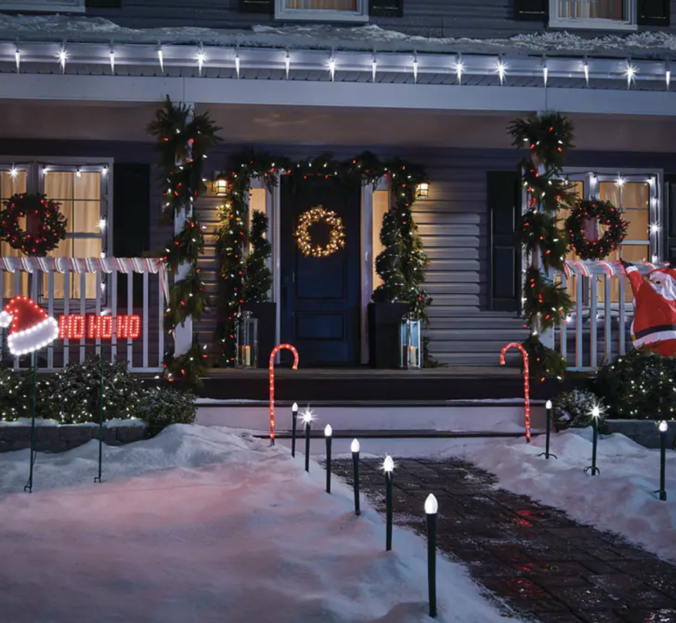 For Living Christmas Lights Candy Cane Stakes in snowy lawn in front of house with christmas decorations (Photo via Canadian Tire)