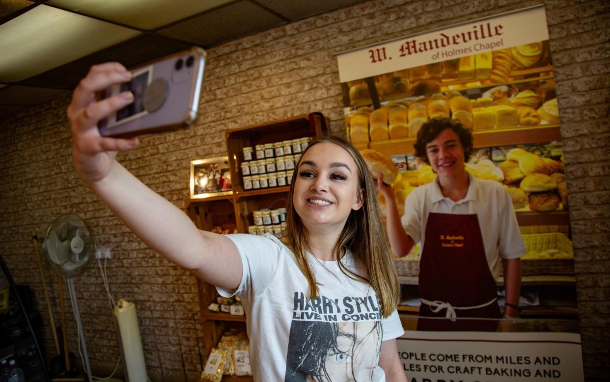 Fan Izzy Hawksworth poses for a selfie in front of a picture of a young Harry Styles proudly displayed at the bakery where he worked