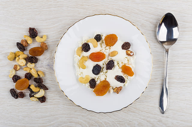 Cottage cheese, sour cream, dried fruits and nuts in plate, spoon, heap of fruits and nuts on wooden table. Top view; Shutterstock ID 1156873687; Purchase Order: N/A