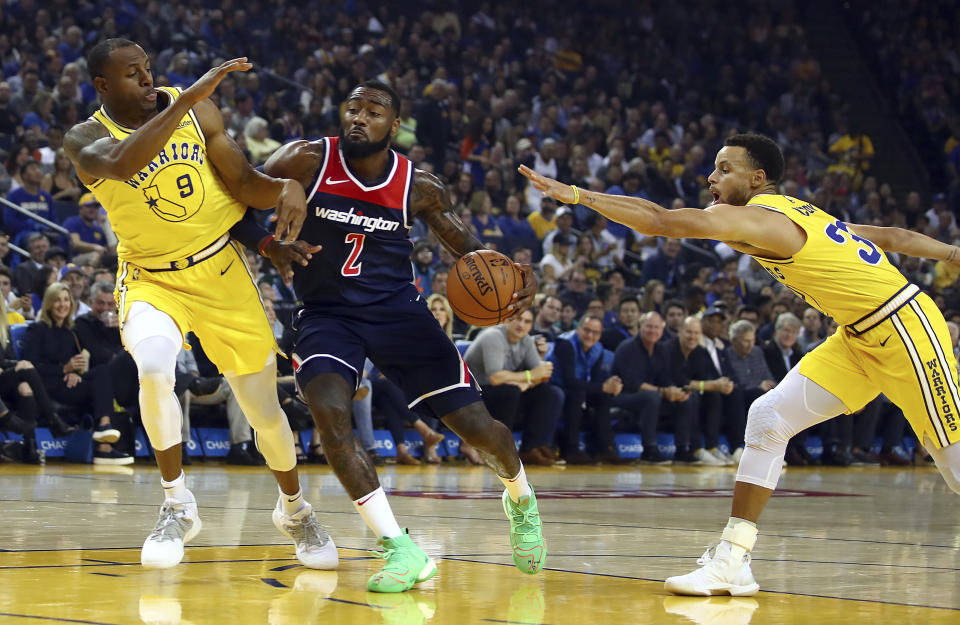 Washington Wizards' John Wall, center, drives the ball between Golden State Warriors' Andre Iguodala, left, and Stephen Curry (30) during the first half of an NBA basketball game Wednesday, Oct. 24, 2018, in Oakland, Calif. (AP Photo/Ben Margot)