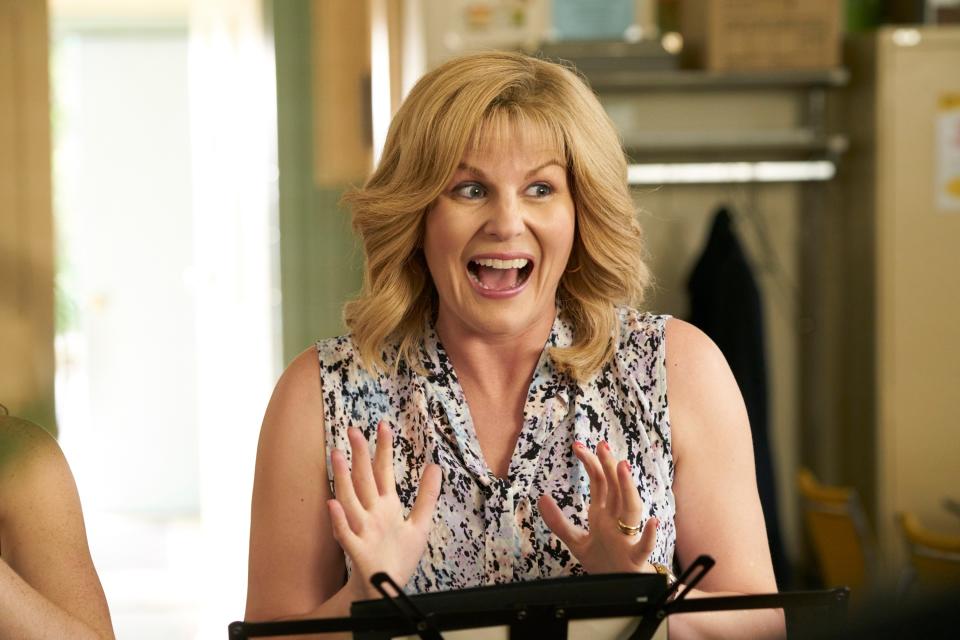 Woman in a patterned top gestures excitedly while standing at a music stand