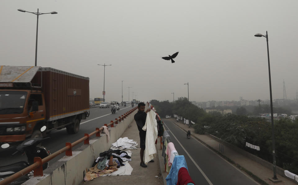 A washerman collects the clothes spread for drying at an over-bridge as city is seen enveloped in thick layer of smog in New Delhi, India, Thursday, Nov. 14, 2019. Schools in India's capital have been shut for Thursday and Friday after air quality plunged to a severe category for the third consecutive day, enveloping New Delhi in a thick gray haze of noxious air. (AP Photo/Manish Swarup)