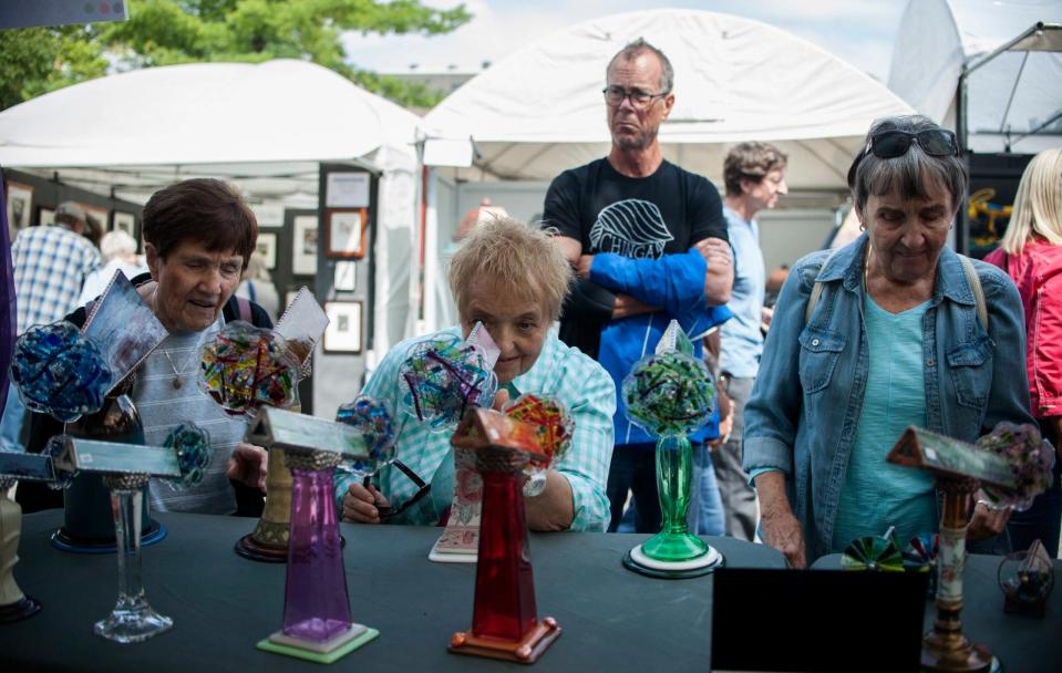 Laurel Keller, center, and other passers-by look through glass kaleidoscopes made by Kathleen Hunt of Conway, South Carolina, during the Fourth Street Festival of the Arts & Crafts in 2017. Some artists and craftspeople from past years will display work alongside new creators during the two-day Labor Day weekend festival.