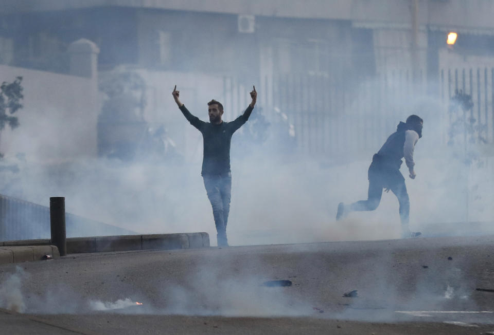 A supporter of the Shiite Hezbollah and Amal Movement groups, stands between the smoke of the tear gas and reacts against the riot police in downtown Beirut, Lebanon, Saturday, Dec. 14, 2019. Lebanon has been facing its worst economic crisis in decades, amid nationwide protests that began on Oct.17 against the ruling political class which demonstrators accuse of mismanagement and corruption. (AP Photo/Hussein Malla)