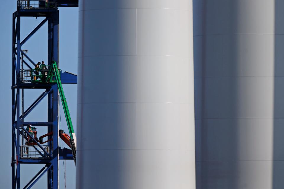 Workmen constructing a steel structure are dwarfed by two wind turbine towers being assembled at the New Bedford Marine Commerce Terminal in New Bedford in this Standard Times file photo.