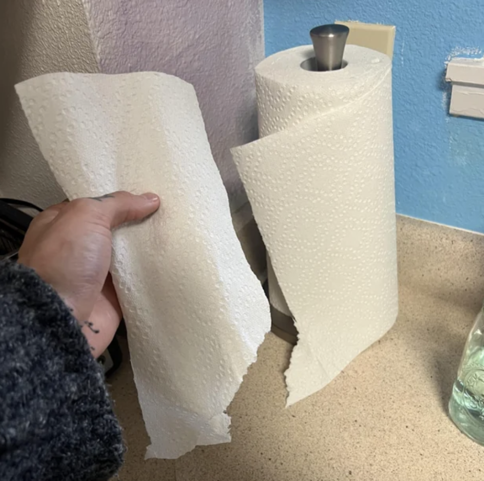 person tearing a paper towel off the roll but it's ripped near the bottom so part of the sheet remains on the roll