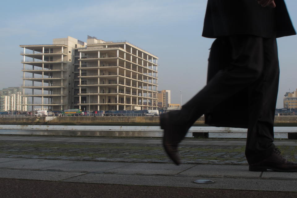 FILE This Thursday, March 22, 2012 file photo shows an Irish commuter walking past the abandoned, unfinished headquarters of Anglo Irish Bank in Dublin. Irish police say detectives have arrested the former chief executive of Anglo Irish Bank and charged him over a conspiracy to hide losses at the bank before its 2009 nationalization. Sean FitzPatrick was arrested Tuesday July 24, 2012 at Dublin Airport as he returned from holiday. The 64-year-old FitzPatrick presided over Ireland's runaway property boom, which was swiftly followed by the banking collapse at the heart of the country's 2010 international bailout. Anglo's losses on bad loans to property speculators are nearing €30 billion ($36 billion), or more than Euros 6,500 ($8,000) for every person in Ireland. Ireland's Justice Department says the 3-year probe into fraudulent practices at Anglo is the biggest in the country's criminal history.(AP Photo/Shawn Pogatchnik, File)