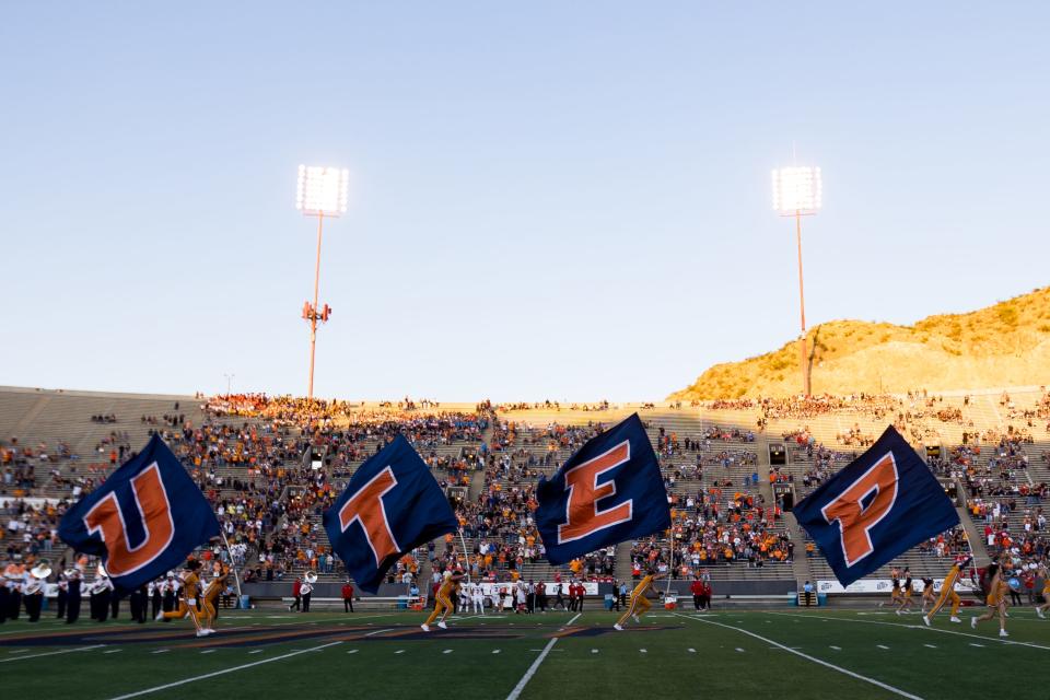 UTEP cheerleaders run down the field with flags that read 