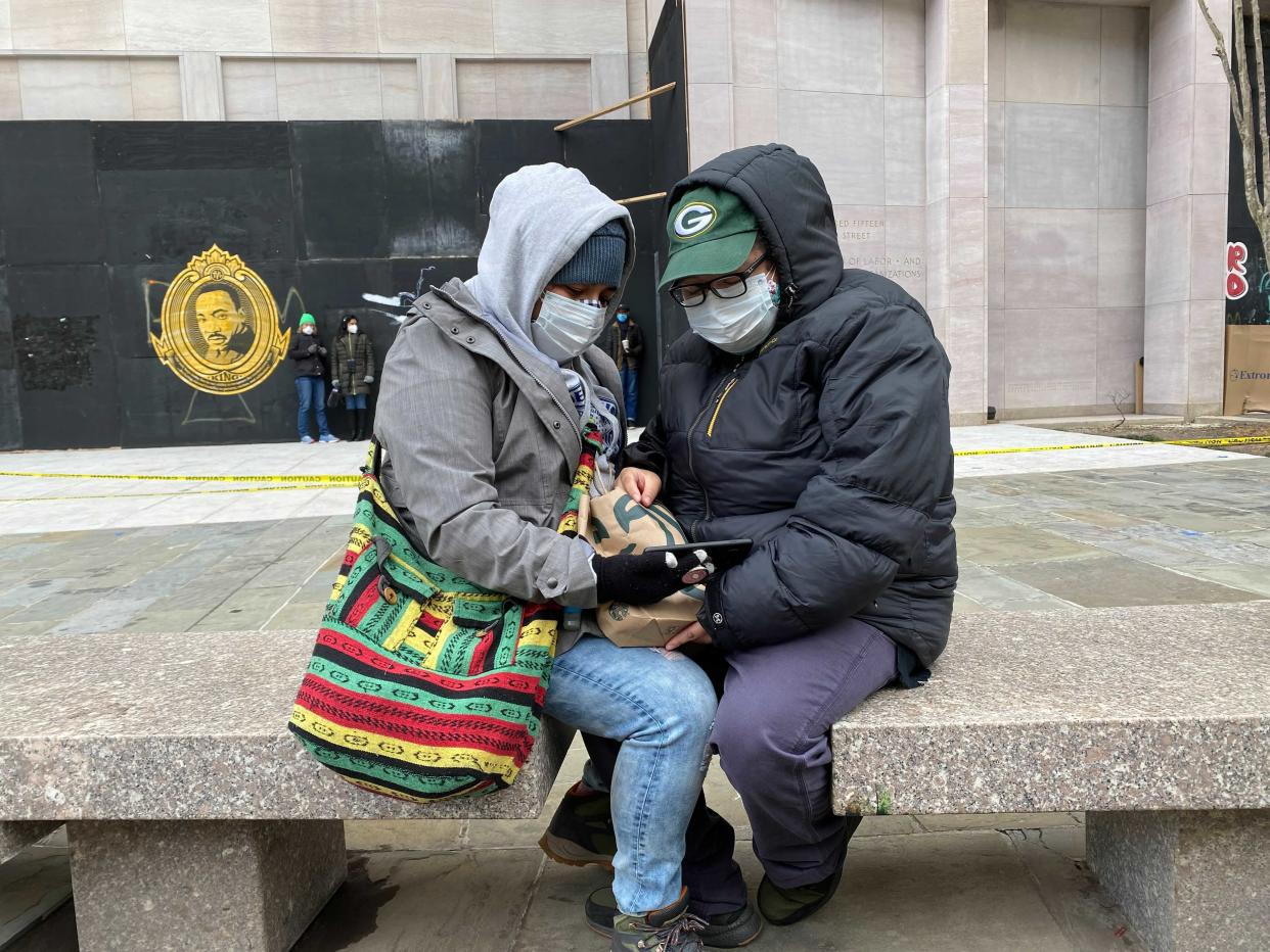 Melissa and Thalia, who gave only their first names, watch Joe Biden’s Inauguration speech in Black Lives Matter Plaza, Washington DC.  (Richard Hall / The Independent)