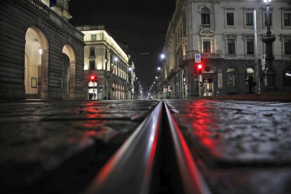 An empty street in front of La Scala opera house is lit by a red traffic light in Milan, northern Italy, early Sunday, Oct. 25, 2020. Since the 11 p.m.-5 a.m. curfew took effect last Thursday, people can only move around during those hours for reasons of work, health or necessity. (AP Photo/Luca Bruno)