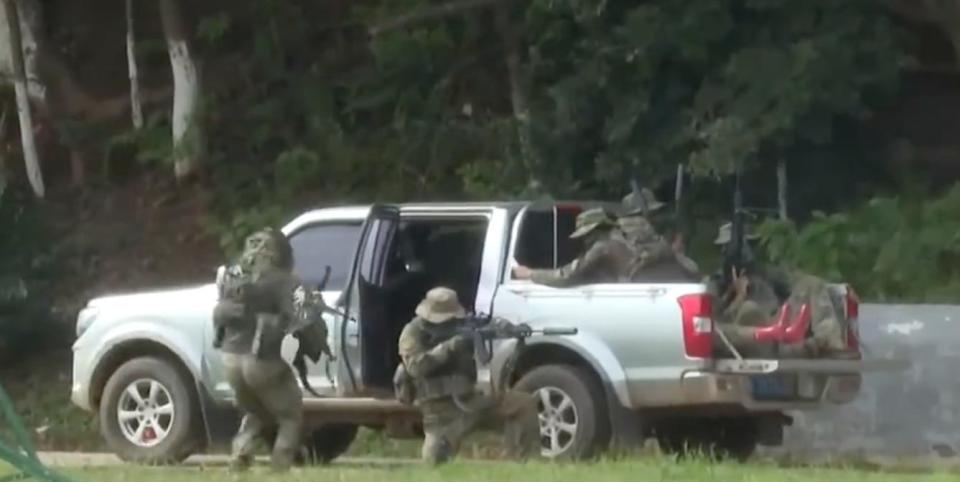 A Chinese commando provides cover fire as his team member enters a pick-up truck.