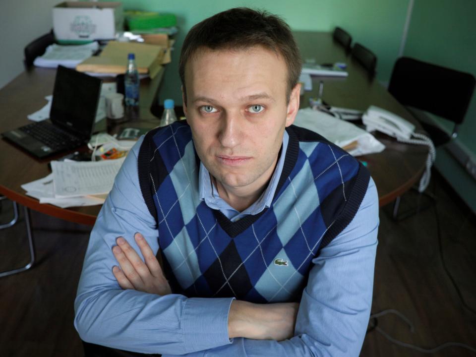 Alexei Navalny, wearing a blue argyle sweater vest and blue shirt, looks up at the camera and poses in his office in Moscow, Russia.