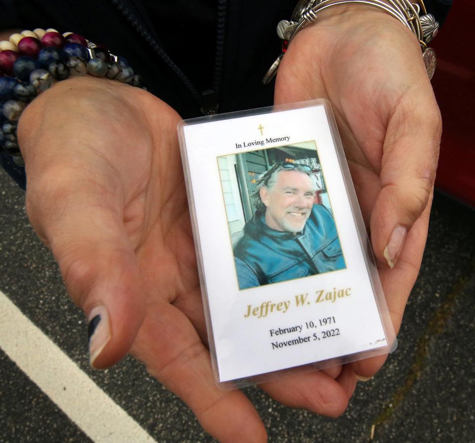 Jessica Edom-Zajac holds the obituary card of her husband Jeffrey in her hands Tuesday, Sept. 26, 2023 as the scene of the crash that took his life in Seabrook in November 2022.