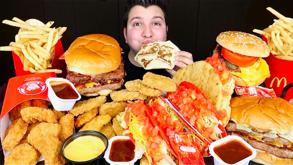 This image taken from video and released by Nikocado Avocado shows him surrounded by items from fast-food chains Wendy's and Taco Bell. Nikocado Avocado, whose real name is Nicholas Perry, 27, has three mukbang channels with 1.71 million subscribers on the largest. He’s a classically trained violinist who gave up that career struggle for mukbang in 2016. (Nikocado Avocado via AP)