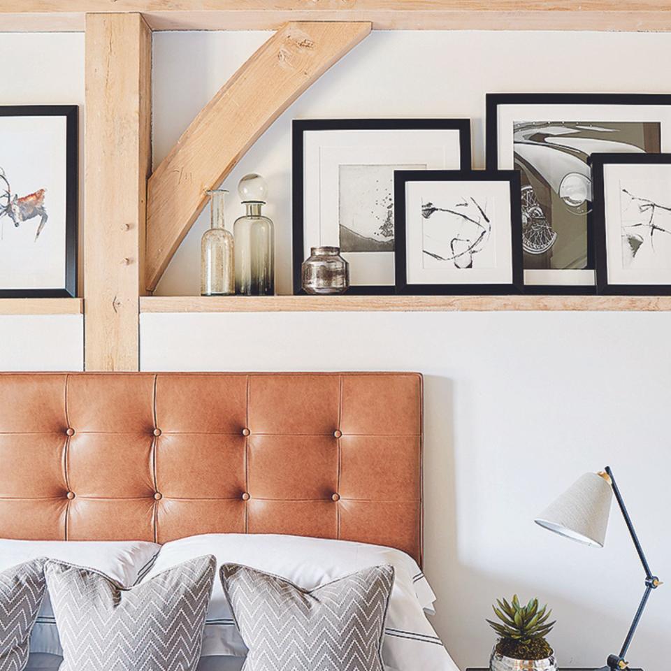 Close up of a bed with a padded leather headboard framed by the pale oak frame and a shelf displaying black and white framed photographs