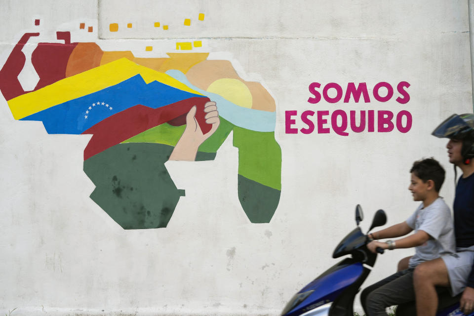 A boy drives a motorcycle in front of a mural of the Venezuelan map with the Essequibo territory included in the 23 de Enero neighborhood of Caracas, Venezuela, Monday, Dec. 11, 2023. Leaders of Guyana and Venezuela are preparing to meet this week to address an escalating dispute over the Essequibo region that is rich in oil and minerals. (AP Photo/Matias Delacroix)