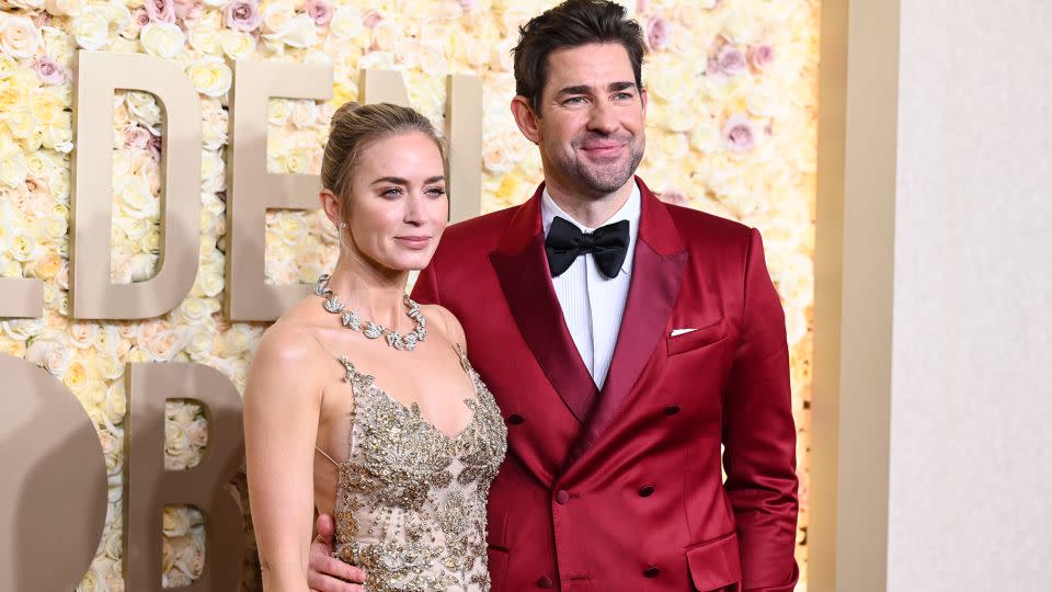 “Oppenheimer” star Emily Blunt wore a gold and white tulle Alexander McQueen dress with Tiffany & Co. jewelry, while husband John Krasinski looked bold in a red satin blazer and burgundy trousers. - Gilbert Flores/Golden Globes/Getty Images