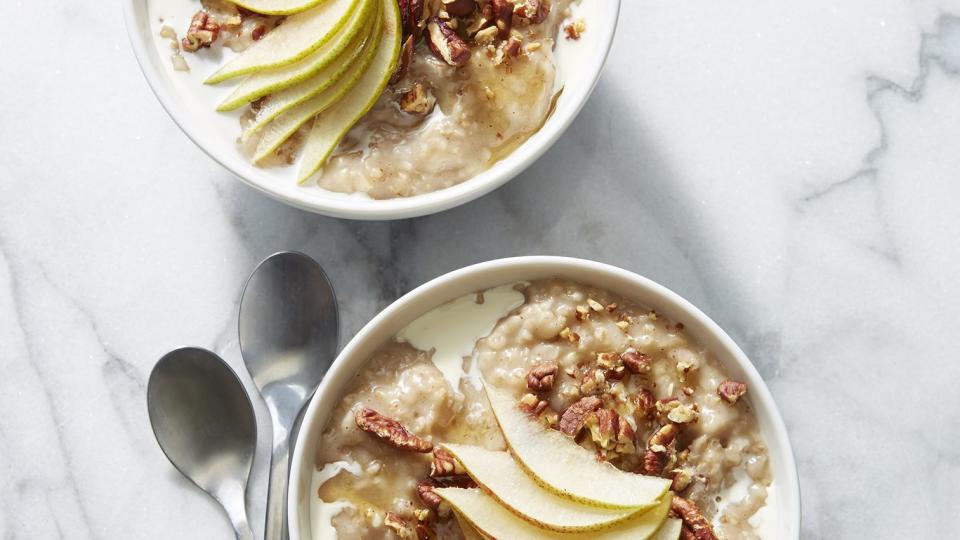 Two bowls of maple, pear, and pecan steel-cut oats displayed on a table with two spoons.