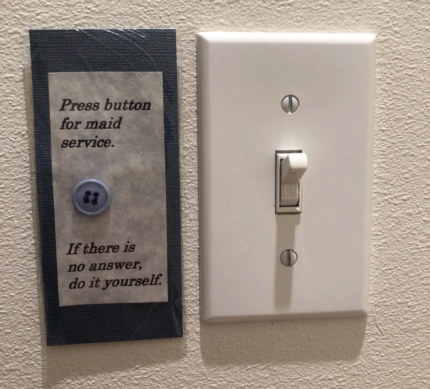 A light switch next to a humorous sign saying, "Press button for maid service. If there is no answer, do it yourself." The "button" is a sewn-on button