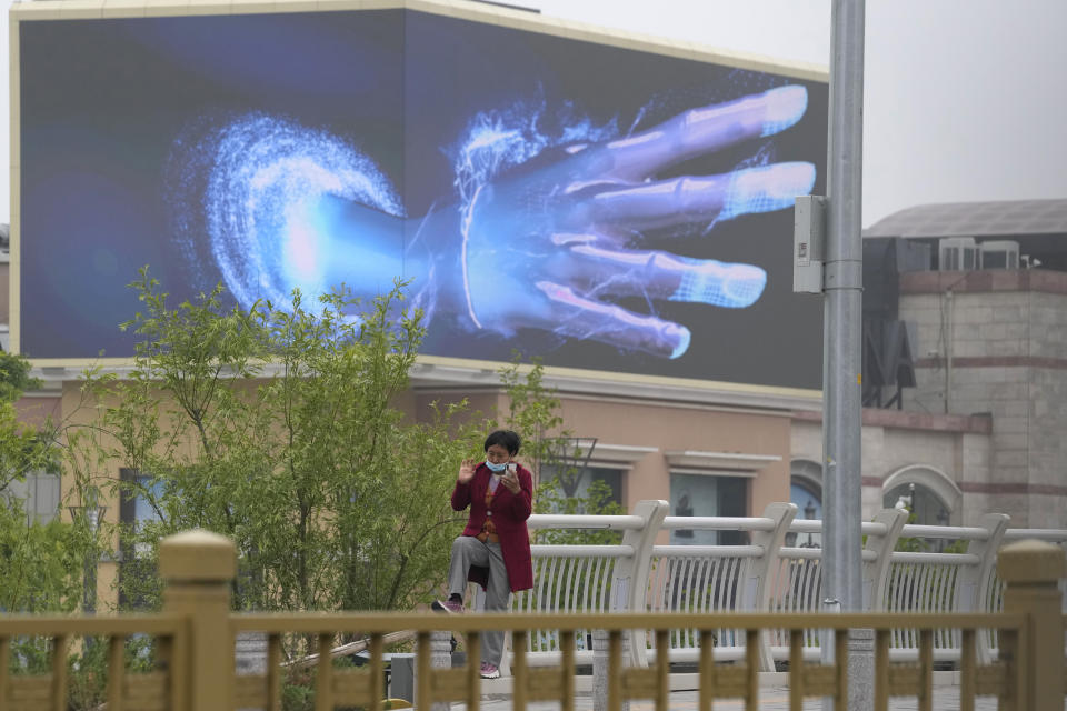 A woman talks on her phone near a screen depicting a giant hand at an empty mall area with closed retail shops and restaurants only offering takeaway on Tuesday, May 10, 2022, in Beijing. China's capital began another round of three days of mass testing for millions of its residents Tuesday in a bid to prevent an outbreak from growing to Shanghai proportions. (AP Photo/Ng Han Guan)