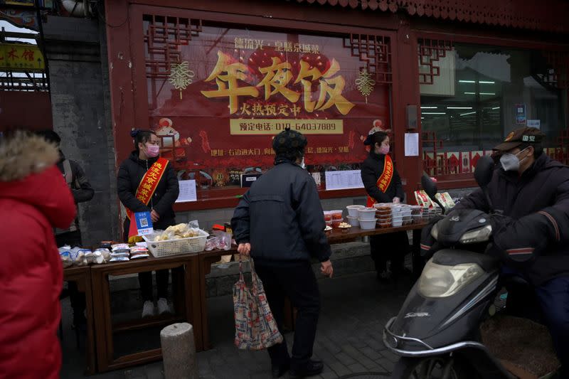 Staff members wearing face masks stand next to a stall set up by a restaurant outside its outlet in Beijing