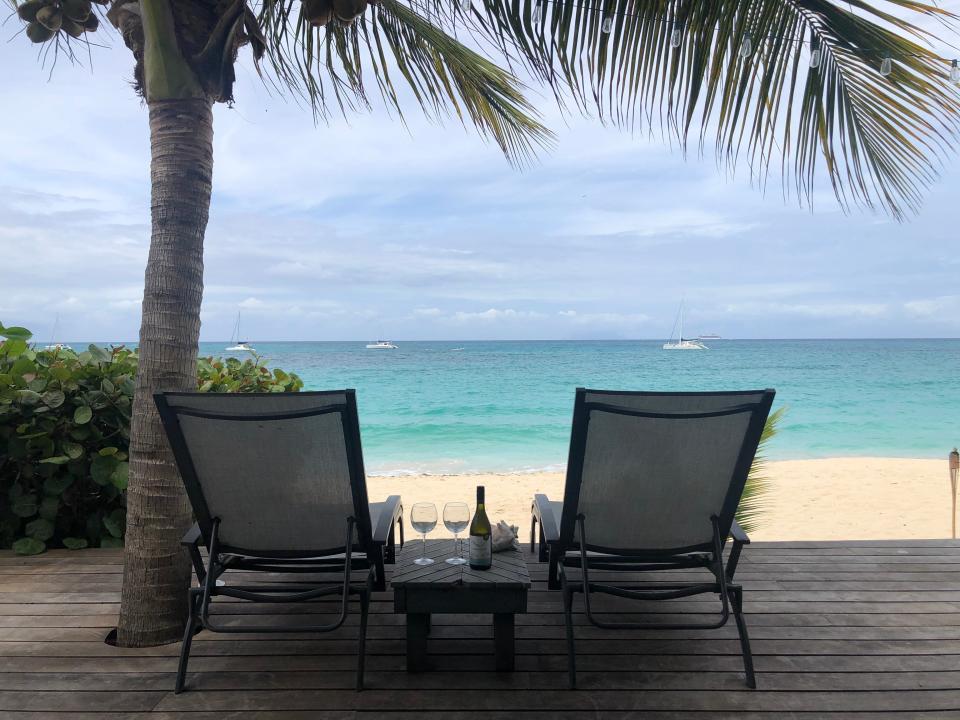 Two chairs under a palm tree on the patio of the beach house.