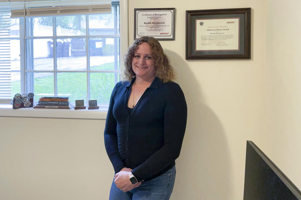 Former longtime BNSF worker Randi Berghorst poses in front of the employee of the year plaque the railroad gave her in recognition of her work supporting LGBTQ+ workers, at her apartment in Woodstock, Ill., in May 2023. Berghorst says that after being promoted regularly earlier in her career she was denied advancement opportunities after her gender transition and could hardly get an interview. (Randi Berghorst via AP)