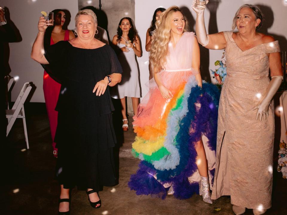 A bride in a rainbow, tulle dress stands with her wedding guests.