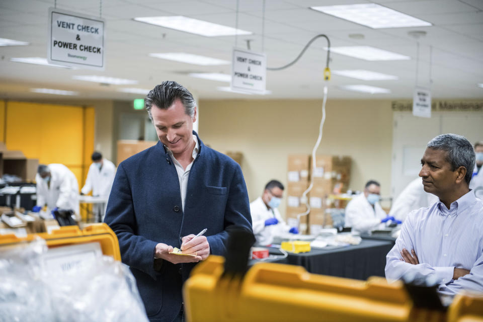 FILE - In this March 28, 2020, file photo, Bloom Energy CEO KR Sridhar, right, watches as California Gov. Gavin Newsom writes down a note during a tour with Sridhar of the Bloom Energy Sunnyvale, Calif., campus. Bloom Energy is a fuel cell generator company that has switched over to refurbishing ventilators as an increasing number of patients experience respiratory issues as a result of COVID-19. Gov. Newsom announced Monday, April 6, 2020, the state would loan 500 ventilators to the national stockpile for use by New York and other states experiencing a crush of coronavirus-related hospitalizations. (Beth LaBerge/Pool Photo via AP, File)