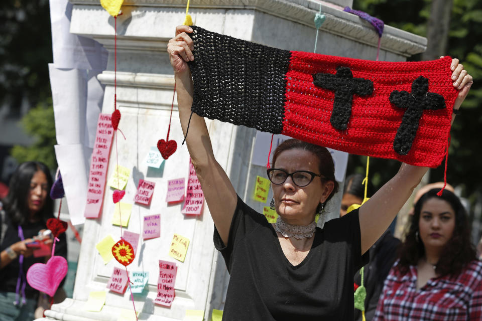 Monica Ortega rises a knitting with black crosses during a tribute for murdered women, in the Alameda park of Mexico City, Saturday, Aug. 24, 2019. A small group of women constructed a memorial made of hand-knit hearts. The knit-in on came on the heels of rowdy protests sparked by outrage over bungled investigations into alleged rapes of teenagers by local policemen. (AP Photo/Ginnette Riquelme)