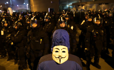 A demonstrators wearing a Guy Fawkes mask on his back stand in front of riot police during a protest against a proposed new labor law, billed as the "slave law", outside the headquarters of the Hungarian state television in Budapest, Hungary, December 17, 2018. REUTERS/Marko Djurica