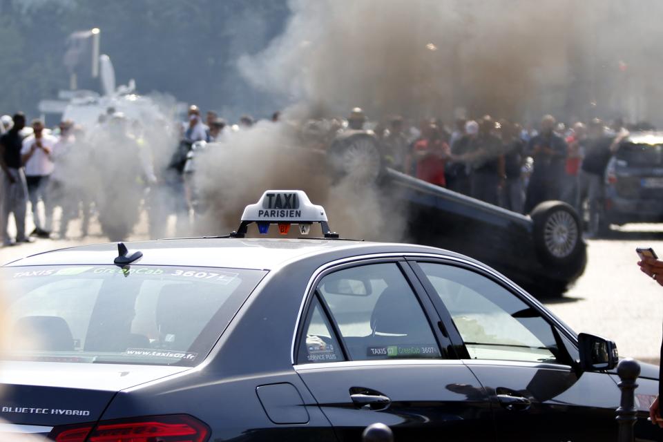 An overturned car is pictured as French taxi drivers, who are on strike, demonstrate at Porte Maillot to block the traffic on the Paris ring road during a national protest against car-sharing service Uber, in Paris, France, June 25, 2015. (REUTERS/Charles Platiau)