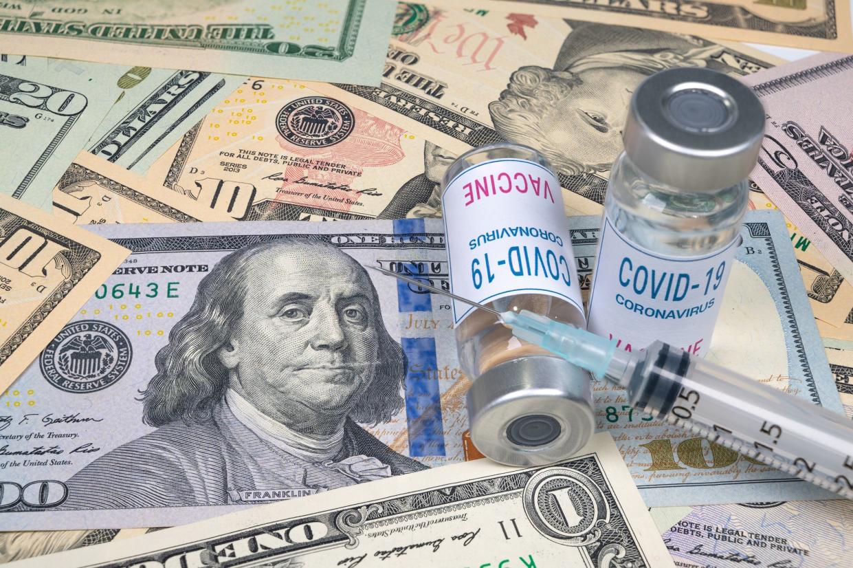 syringes and covid-19 vaccine ampoule lying on top of the US dollar.