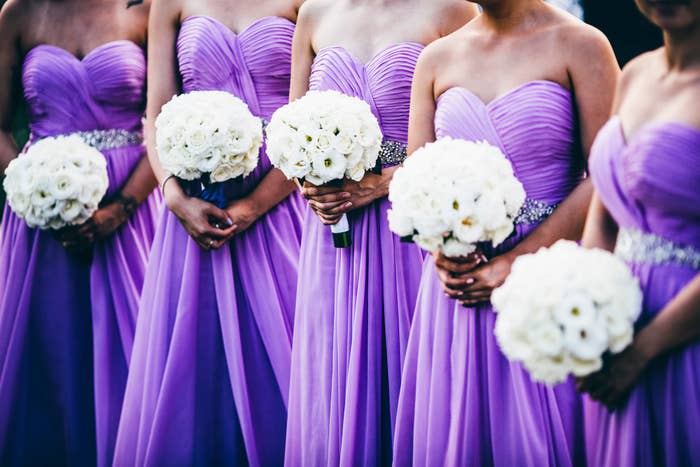 Five women in matching strapless gowns hold white rose bouquets. Names not available