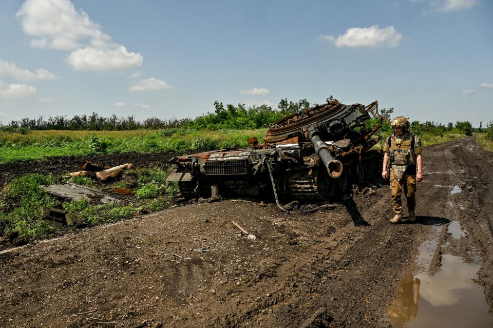 A press officer looks at a destroyed Russian military vehicle in a muddy field.