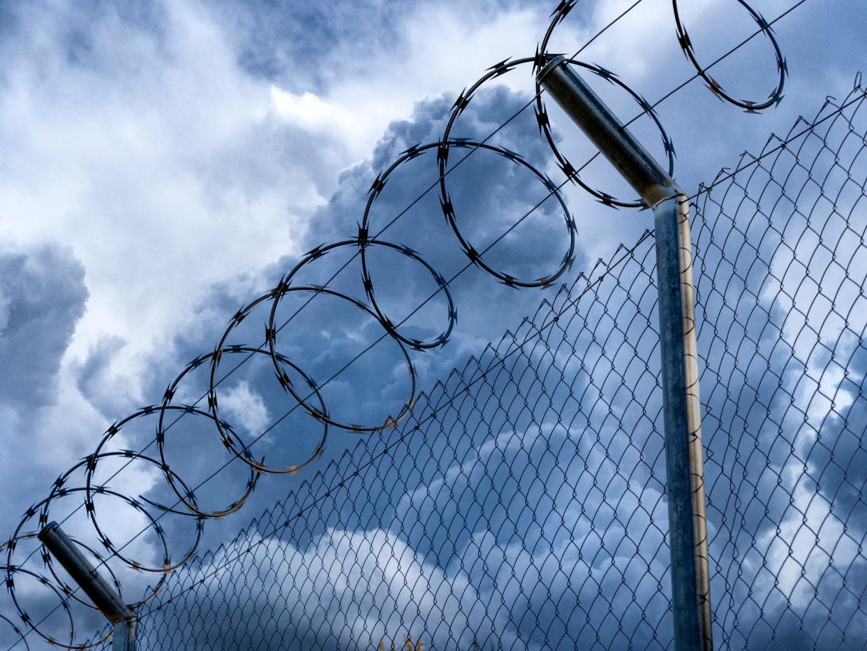 Close-up of metal fence with barbed wire over a stormy blue sky