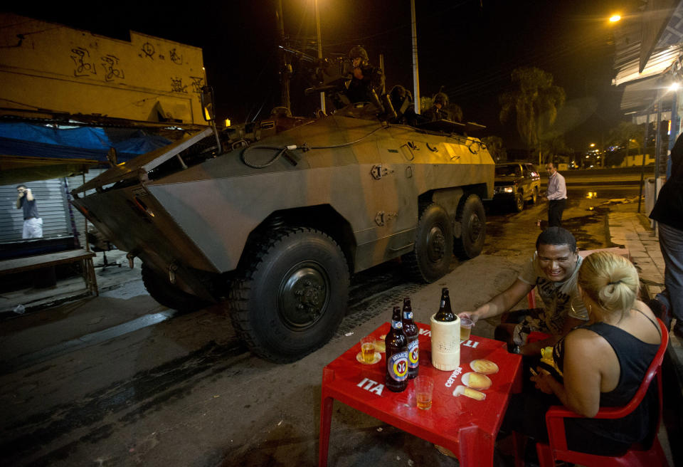 A couple drink beer while Army soldiers enter to occupy the Mare slum complex in Rio de Janeiro, Brazil, Saturday, April 5, 2014. More than 2,000 Brazilian Army soldiers moved into the Mare slum complex early Saturday in a bid to improve security and drive out the heavily armed drug gangs that have ruled the sprawling slum for decades. (AP Photo/Silvia Izquierdo)