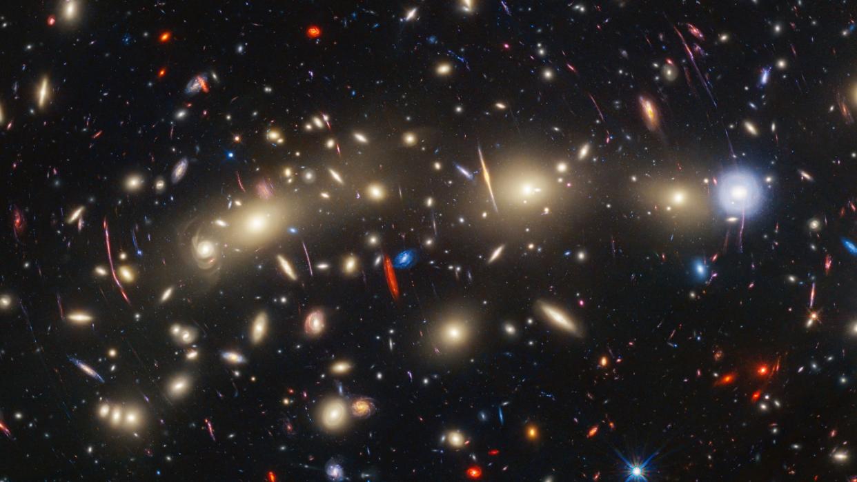  We see an array of twinkling yellow, red, and blue galaxies stretched across space in a way that is reminiscent of Christmas lights. 