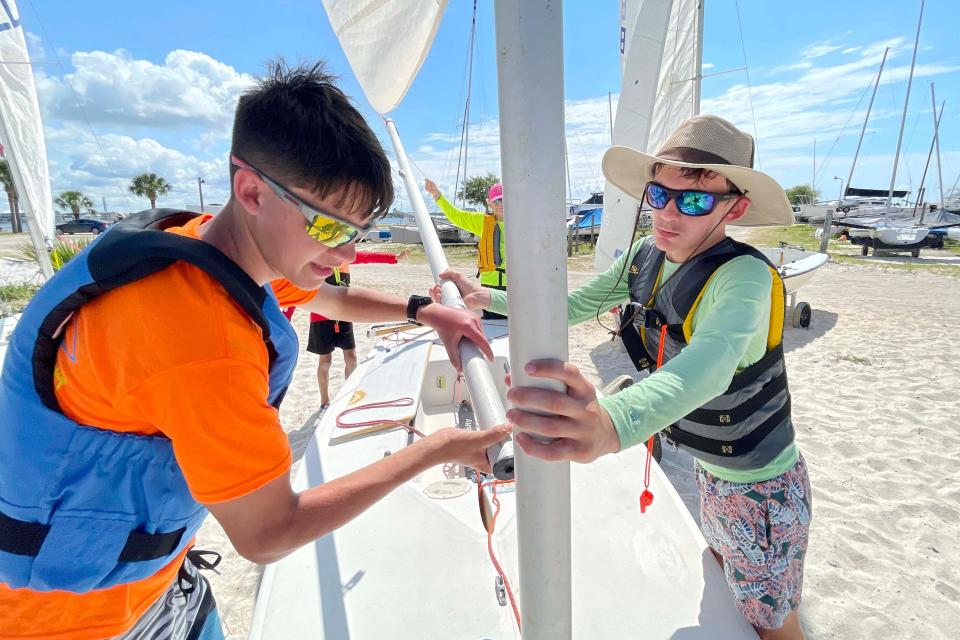 Sailing instructor Logan Snyder (left) helps student Samuel Adams rig his sail at the Fort Walton Yacht Club this week during one of the Emerald Coast Sailing Association's summer camps.