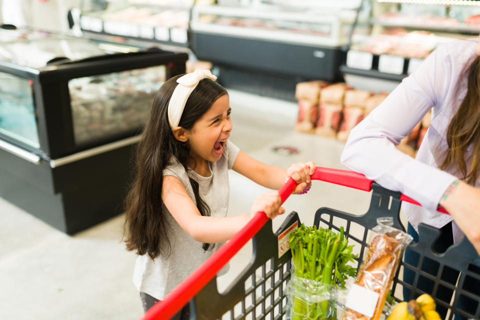 chlid screaming while holding a shopping cart in a grocery store