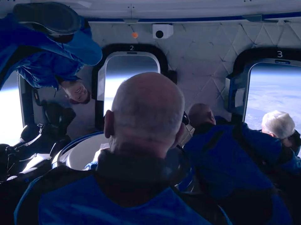 jeff bezos and three other passengers in jumpsuits float around spaceship cabin earth in background