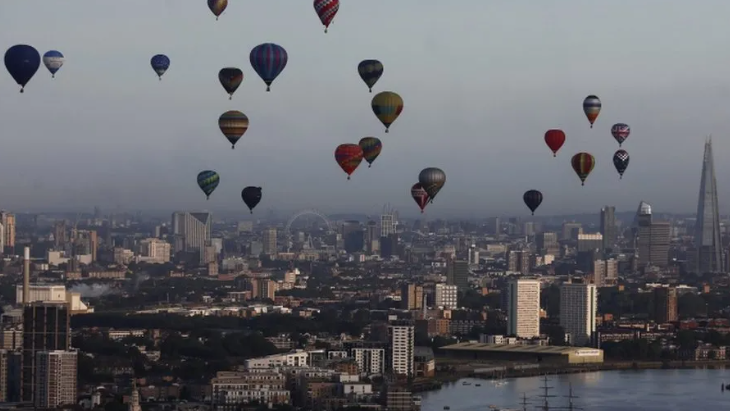 Hot air balloons soar above central London with the River Thames in the foreground and the Shard, Eye and other buildings are in the background