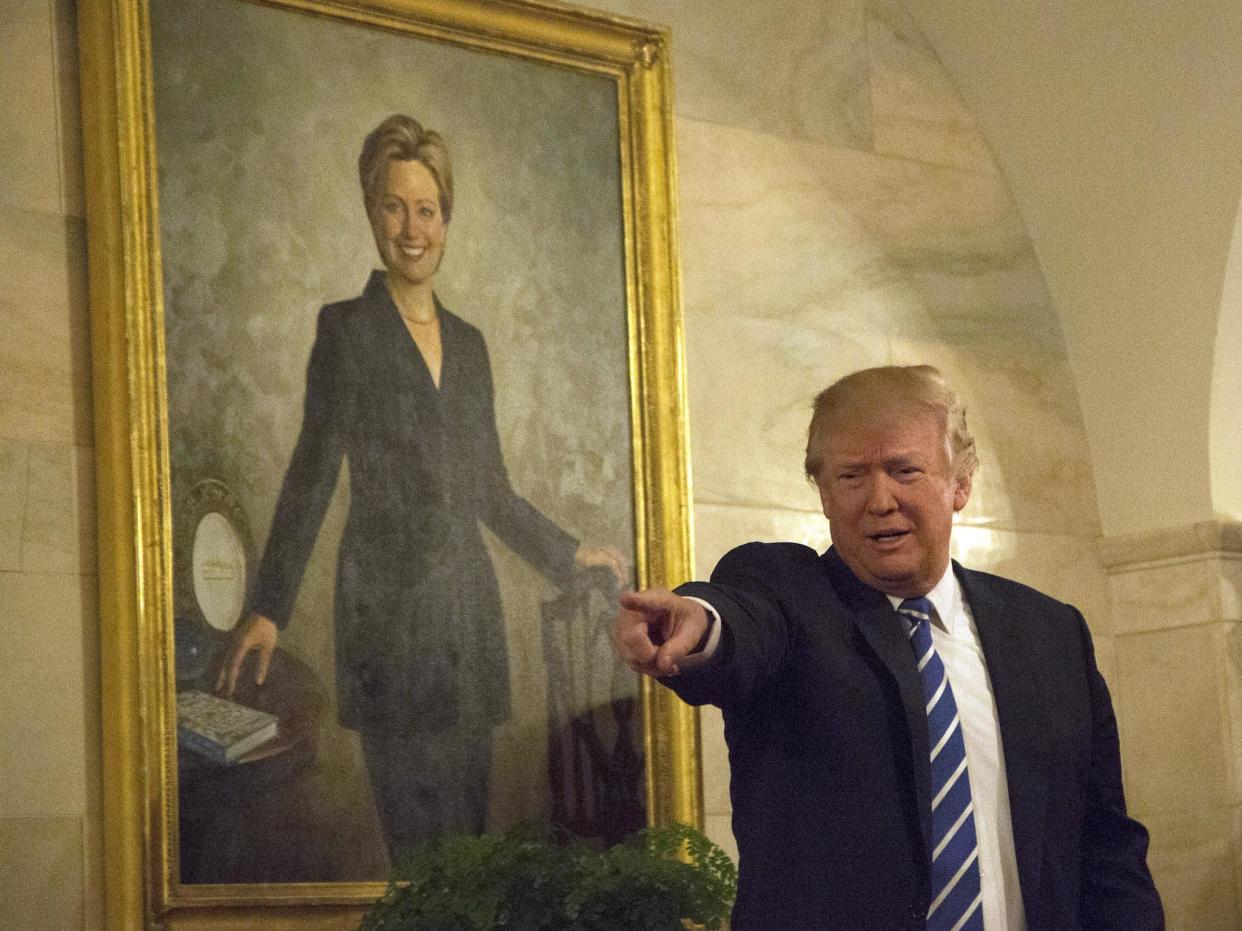 US President Donald Trump walks in a corridor of the White House to greet visitors, while a portrait of Hillary Clinton hangs on the wall, March 7, 2017 in Washington, DC: Getty Images