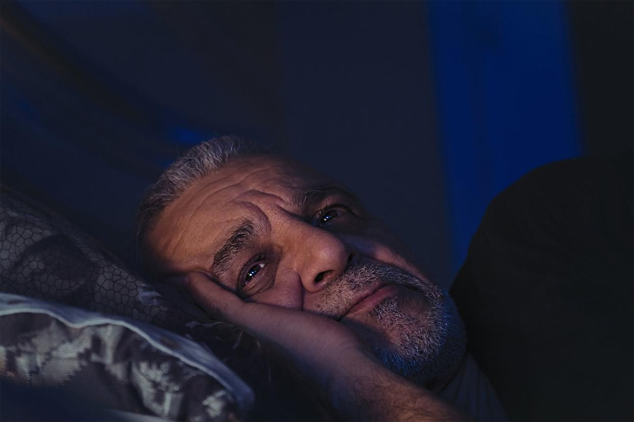 Closeup of worried senior man's face while laying on pillow, he is laying on his bed on his side, looking up, dark blues and blacks in the image